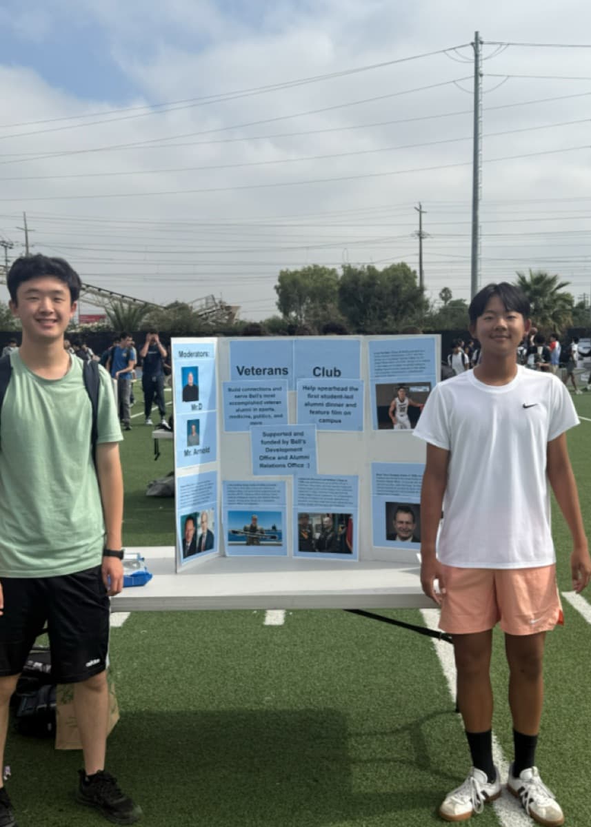 Two students standing beside the Veterans Club display board at Club Day.